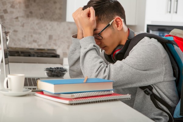 Stressed student at a desk with books.